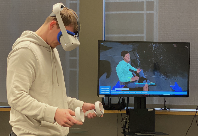 A male student uses a VR headset and hand controllers in an emergency response VR simulation