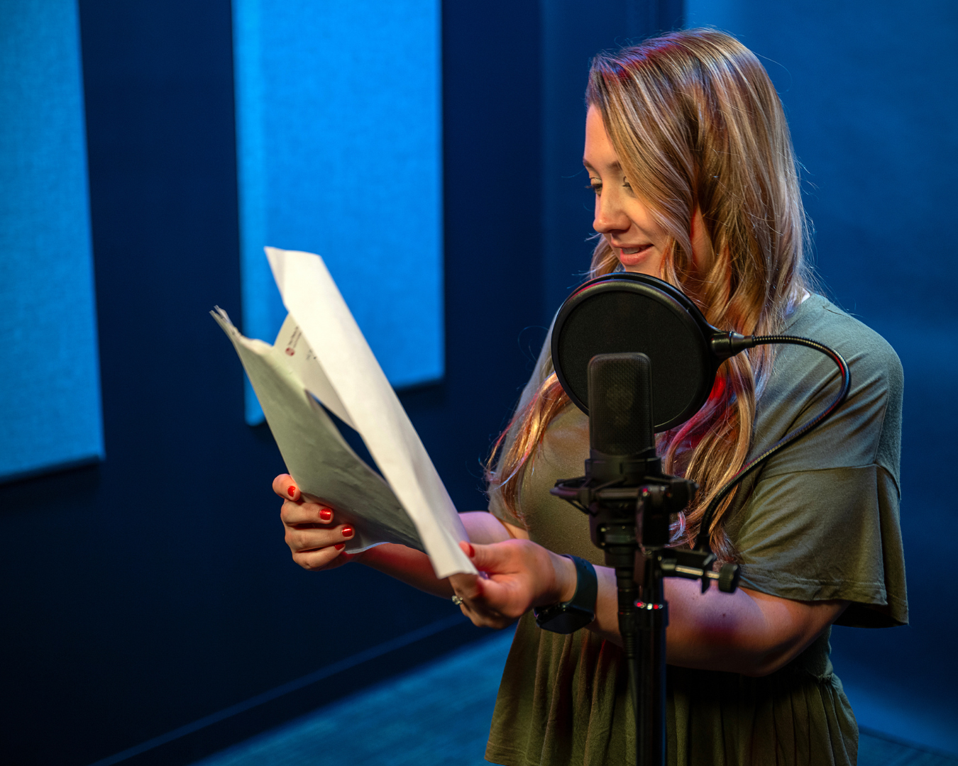 Young woman reading script into microphone.