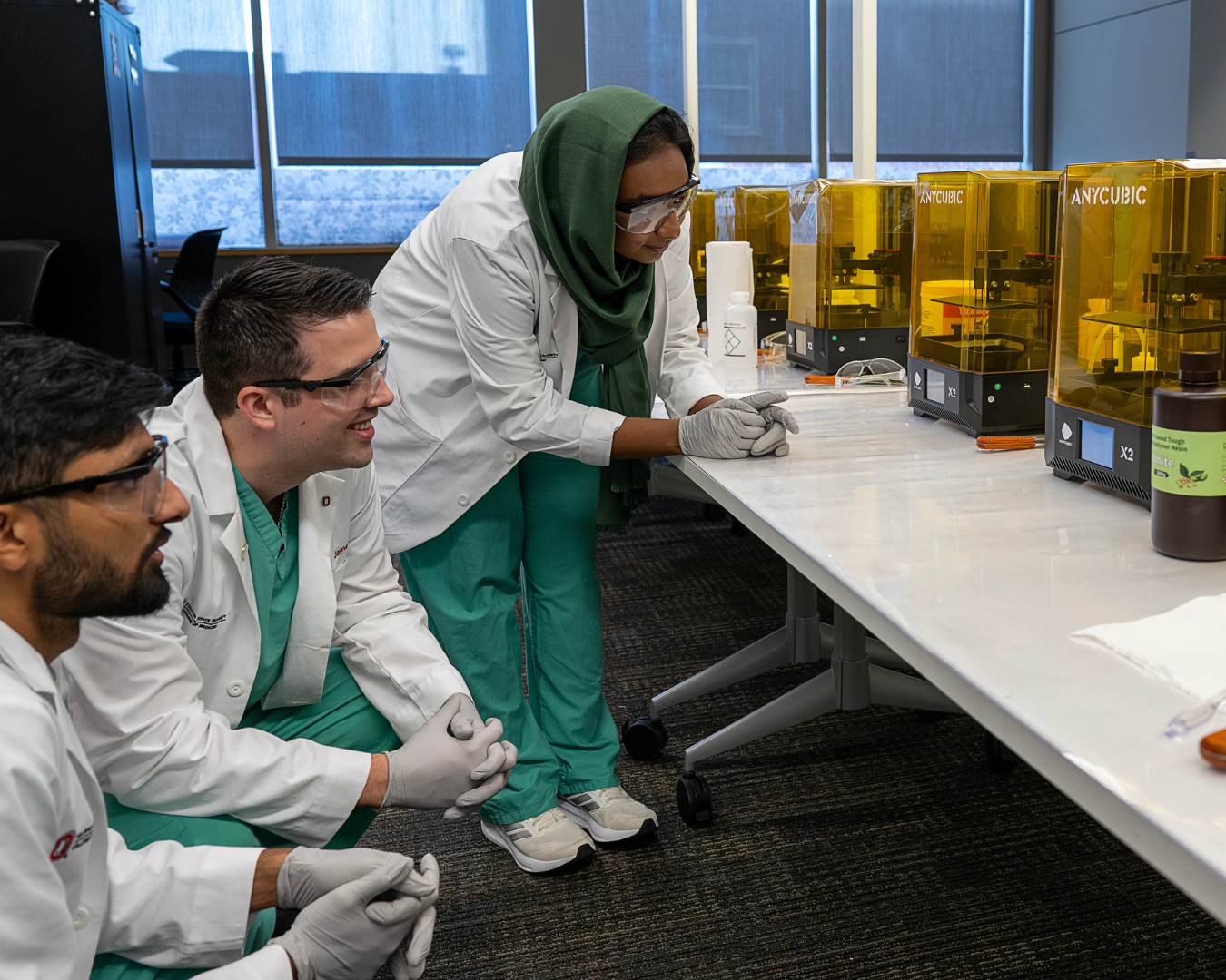 Image of 3 medical students watching the 3-D printer develop a model.