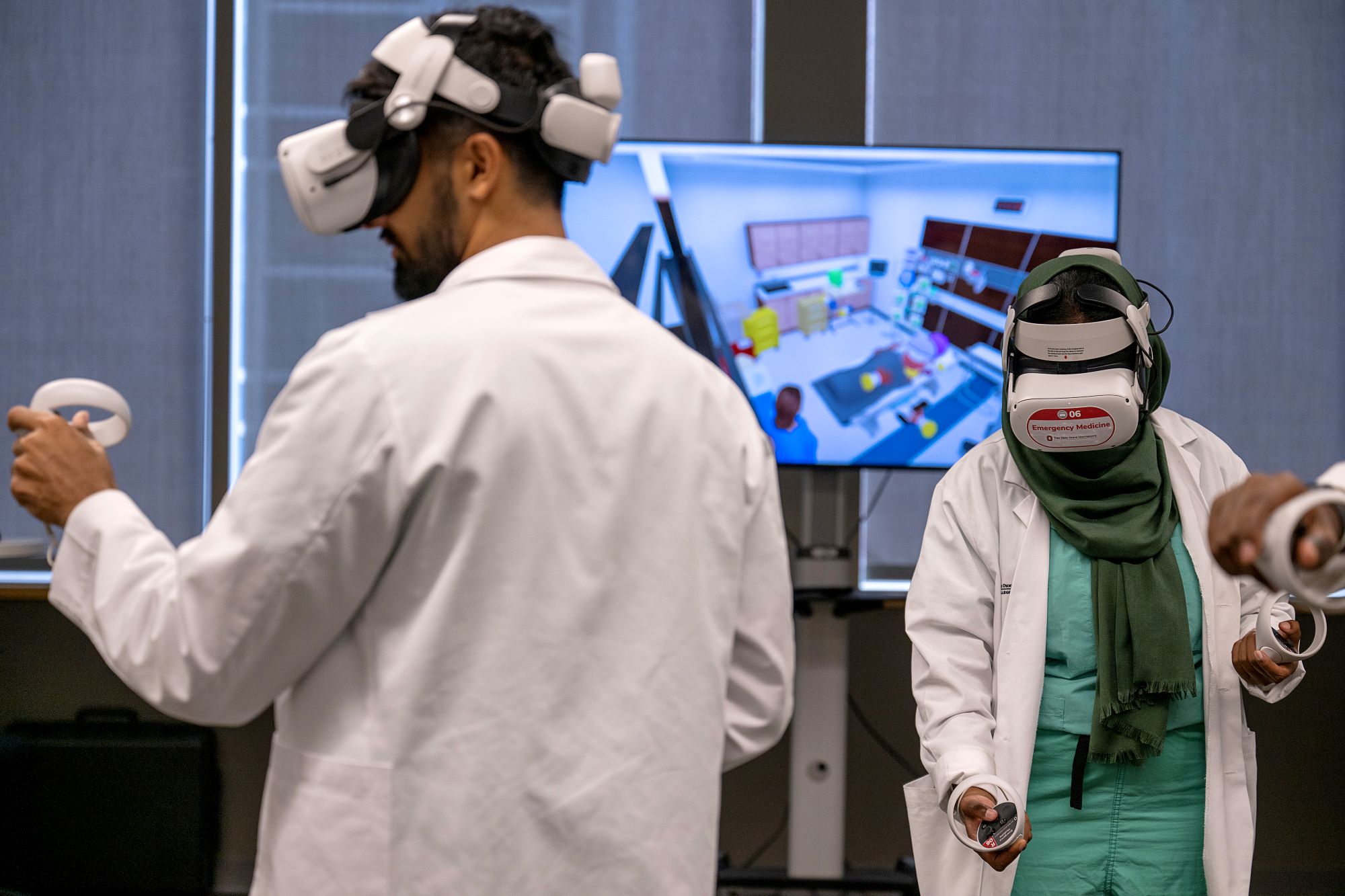 Two students wearing scrubs and lab coats, both interacting within the same virtual reality hospital scenario.