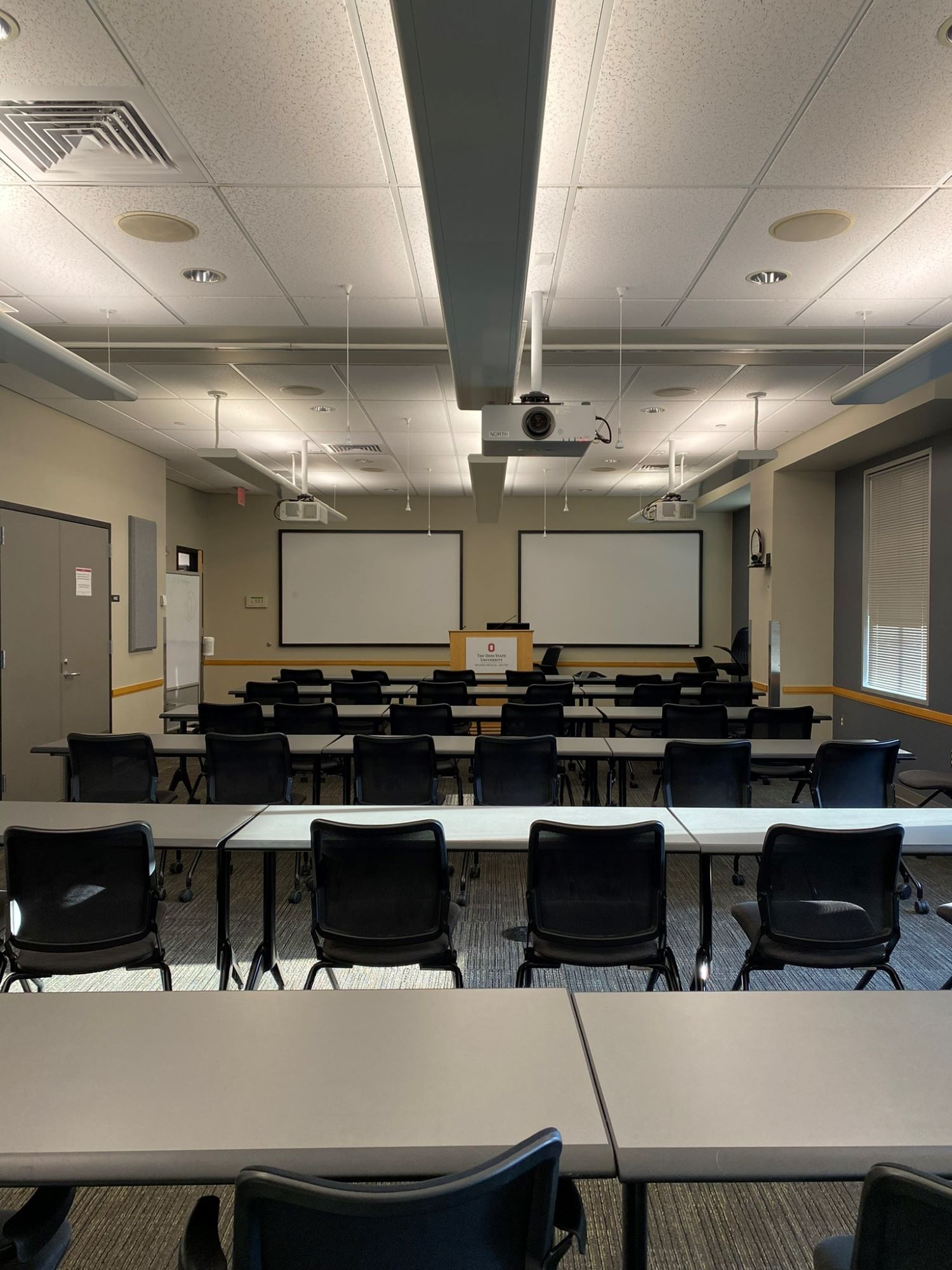 Interior of the Tech-Equipped Classroom featuring several rows of desks and two projection screens on one wall.