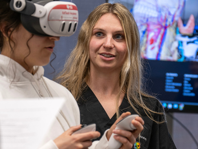 An Ohio State faculty member assists a student wearing a VR headset and hand controllers during a classroom exercise