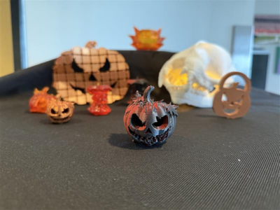 A decorative black jack-o'-lantern sits on a table, surrounded by various Halloween-themed sculptures, including a skull and pumpkin shapes, creating a spooky atmosphere.