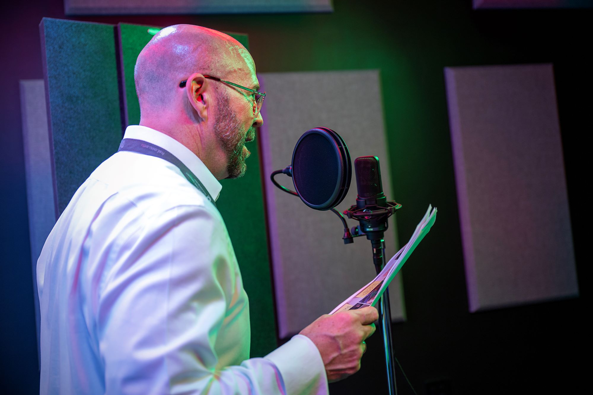 A man speaking into a microphone within THE Studio's recording booth while holding a script.