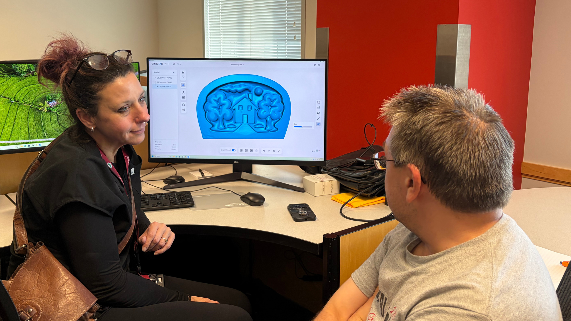 Two people talking in front of a computer that displays a 3D model.