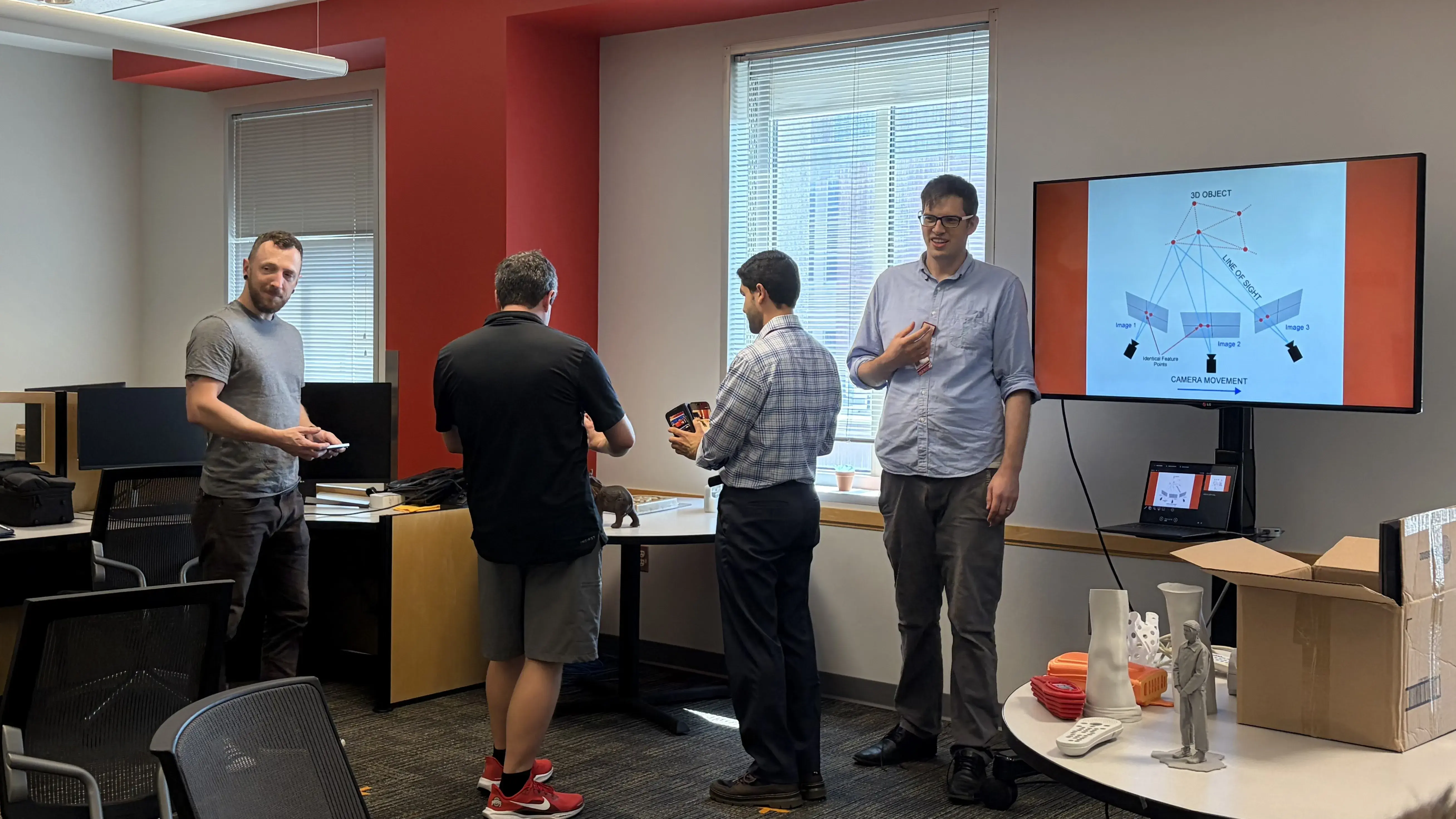 Thomas presenting about 3D scanning while a group works beside him to scan an object.